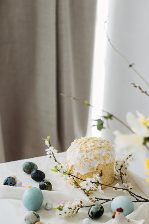 Stylish easter eggs, panettone and spring flowers on linen cloth on rustic table. Natural dye eggs and cherry blossom, festive minimal still life. Happy Easter!の写真素材