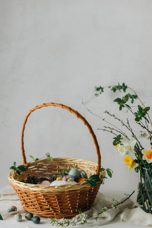 Stylish Easter basket with eggs and food with spring flowers on rustic table. Happy Easter! Traditional easter holiday food. Modern natural dye eggs, tasty ham, bread, butter, beetsの写真素材