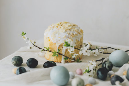 Stylish easter eggs, panettone and spring flowers on linen cloth on rustic table. Natural dye eggs and cherry blossom, festive minimal still life. Happy Easter!の写真素材