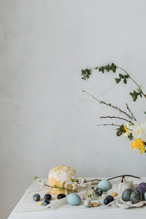 Happy Easter! Stylish easter eggs, homemade easter bread and spring flowers on linen napkin on rustic table against wall. Natural painted blue and marble eggs and cherry blooms still lifeの写真素材