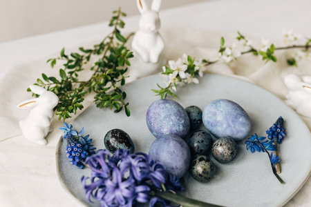 Stylish easter eggs on vintage plate, bunny and spring flowers on rustic table. Happy Easter! Natural dye blue eggs, purple hiacynt blossoms on linen napkin. Holiday setting, minimal still lifeの写真素材