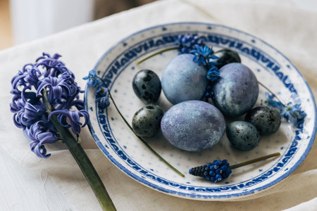Happy Easter! Stylish easter eggs on vintage plate and spring flowers on linen napkin, rustic table setting. Natural painted blue eggs and hyacinth blooms. Modern minimal still lifeの写真素材