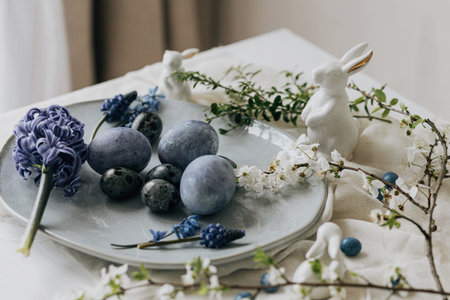 Happy Easter! Stylish easter eggs on vintage plate, bunny and spring flowers on linen napkin, rustic table setting. Natural painted blue eggs and hyacinth blooms. Modern minimal still lifeの写真素材