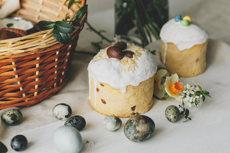 Stylish Easter bread, eggs and basket with food with spring flowers on rustic table. Happy Easter! Traditional easter holiday food. Modern natural dye eggs and daffodils and cherry blossomの写真素材
