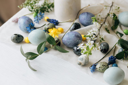 Stylish easter eggs and spring flowers on rustic wooden table. Happy Easter! Natural dye marble and blue eggs, purple hiacynt blossoms and daffodils. Minimal still life.の写真素材