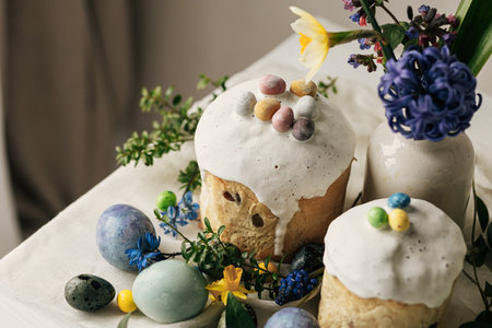 Happy Easter! Stylish easter eggs, homemade easter bread and spring flowers on linen napkin on rustic table. Natural painted marble eggs, blooms and holiday food. Modern still lifeの写真素材