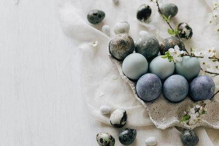 Happy Easter! Stylish easter eggs and spring flowers on linen rustic table. Natural painted marble blue eggs in tray and cherry blooms. Modern minimal flat layの写真素材