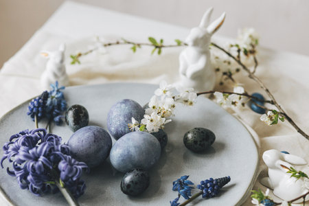 Happy Easter! Stylish easter eggs on vintage plate, bunny and spring flowers on linen napkin, rustic table setting. Natural painted blue eggs and hyacinth blooms. Modern minimal still lifeの写真素材