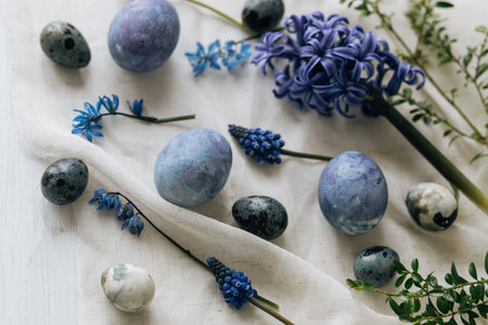 Stylish easter eggs and spring flowers on rustic wooden table. Happy Easter! Natural dye marble and blue eggs, purple hiacynt blossoms on linen. Minimal flat layの写真素材