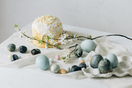 Happy Easter! Stylish easter eggs, homemade easter bread and spring flowers on linen napkin on rustic table against wall. Natural painted blue and marble eggs and cherry blooms still lifeの写真素材