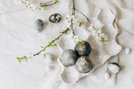 Happy Easter, flat lay. Stylish easter eggs and spring flowers on linen rustic table. Natural painted marble eggs in tray and cherry blooms. Modern minimal flat layの写真素材
