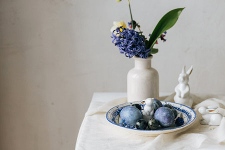 Stylish easter eggs on vintage plate, bunny and spring flowers on rustic table. Happy Easter! Natural dye blue eggs, purple hiacynt blossoms on linen napkin. Holiday setting, minimal still lifeの写真素材