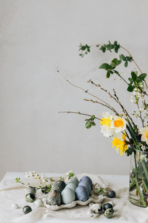 Happy Easter! Stylish easter eggs and spring flowers on linen rustic table. Natural painted marble blue eggs in tray and daffodils bouquet. Modern minimal still lifeの写真素材