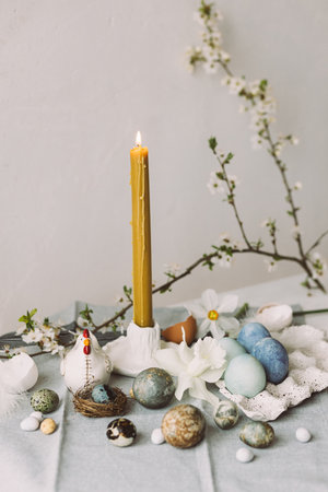 Stylish easter eggs in tray, cherry blossom and candle on rustic table. Happy Easter! Modern natural...