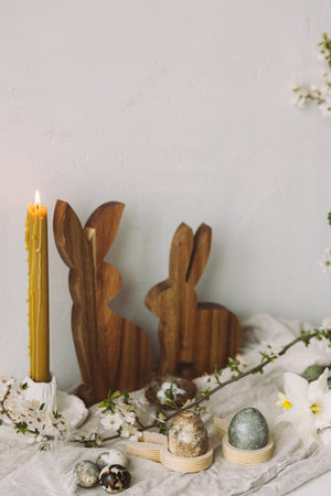 Stylish easter eggs, wooden bunnies, cherry blossom and candle composition on rustic table. Happy...