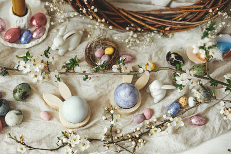 Happy Easter! Stylish easter eggs, bunnies and cherry blossom  flat lay on rustic table. Modern natural dyed and chocolate colorful eggs and spring flowers. Easter still life  in countrysideの写真素材