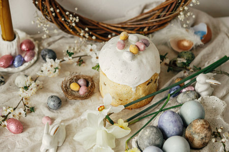 Stylish easter eggs, panettone, bunnies, cherry blossom and daffodils composition on rustic table. Happy Easter! Modern natural dyed eggs, festive food and spring flowers still lifeの写真素材