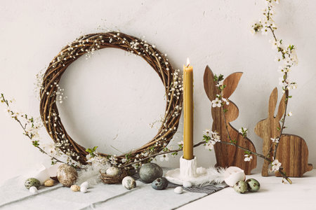 Happy Easter! Stylish easter eggs, wooden bunnies, cherry blossom and candle on rustic table. Modern natural dyed marble eggs and spring flowers. Easter still life decor in countryside homeの写真素材