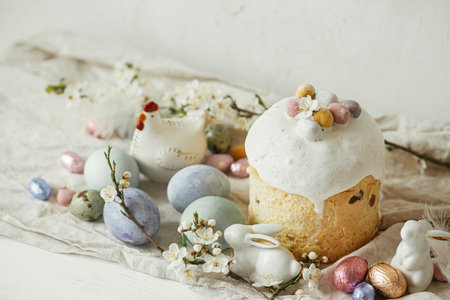 Stylish easter eggs, panettone, bunnies, cherry blossom composition on rustic table. Happy Easter! Modern natural dyed eggs, festive food and spring flowers. Rural still lifeの写真素材