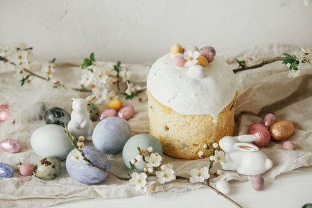 Stylish easter eggs, panettone, bunnies, cherry blossom composition on rustic table. Happy Easter! Modern natural dyed eggs, festive food and spring flowers. Rural still lifeの写真素材