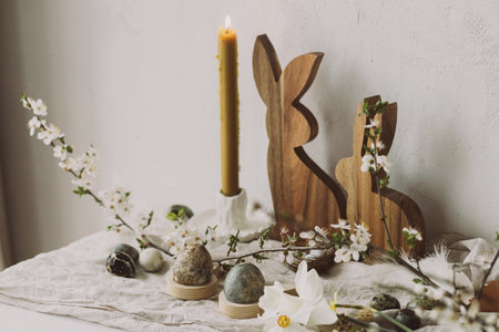 Stylish easter eggs, wooden bunnies, cherry blossom and candle composition on rustic table. Happy...