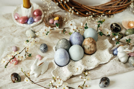 Happy Easter! Stylish easter eggs, bunnies and cherry blossom on rustic table. Modern natural dyed and chocolate colorful eggs and spring flowers. Easter still life decor in countryside homeの写真素材