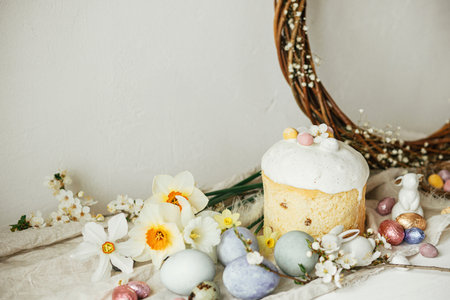 Stylish easter eggs, panettone, bunnies, cherry blossom and daffodils composition on rustic table. Happy Easter! Modern natural dyed eggs, festive food and spring flowers still lifeの写真素材