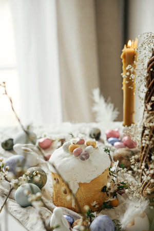 Stylish easter eggs, panettone, bunnies, cherry blossom and daffodils composition on rustic table....