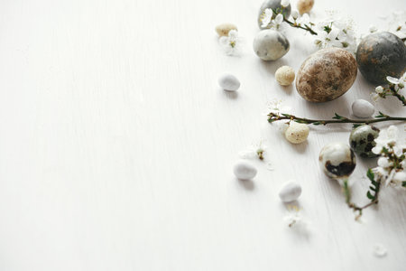 Stylish easter eggs and cherry blossom on rustic white table. Happy Easter! Minimal easter border template with space for text. Modern natural dye marble eggs and spring flowersの写真素材