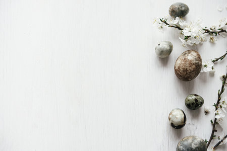 Easter flat lay. Stylish easter eggs and cherry blossom on rustic white table. Happy Easter! Minimal easter border template with space for text. Modern natural dye marble eggs and spring flowersの写真素材