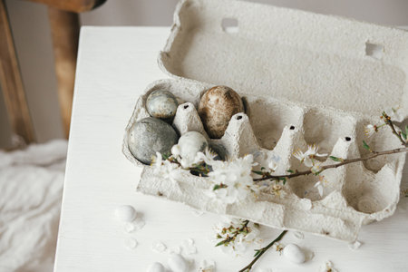 Happy Easter! Stylish easter eggs in tray and cherry blossom on rustic  table. Modern natural dye marble eggs and spring flowers still life. Rural easter compositionの写真素材