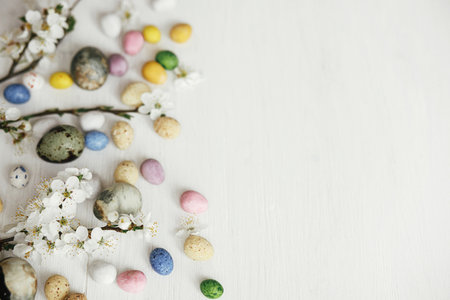 Easter flat lay. Stylish easter eggs and cherry blossom on rustic white table. Happy Easter! Easter border with space for text. Modern dye marble and colorful chocolate eggs and spring flowersの写真素材