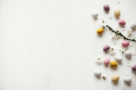 Easter flat lay. Stylish easter chocolate eggs and cherry blossom on rustic white table. Happy Easter! Easter border with space for text. Modern candy colorful eggs and spring flowersの写真素材