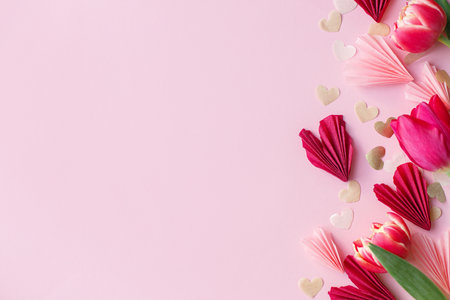 Stylish hearts and tulips on pink background flat lay. Happy Valentines day and happy mothers day. Valentine  border with pink, red and gold hearts paper cutouts. Banner template, space for textの写真素材