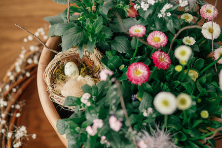 Stylish easter eggs with feather in nest and potted spring flowers composition top view on table. Happy Easter! Simple easter table setting decor in farmhouse living roomの写真素材