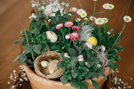 Stylish easter eggs with feather in nest and potted spring flowers composition close up on table. Happy Easter! Simple easter table setting decor in farmhouse living roomの写真素材
