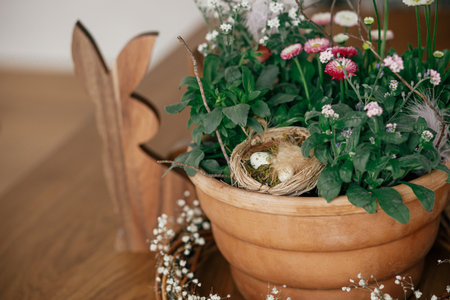 Stylish easter eggs with feather in nest, potted spring flowers  and bunny figurines composition on wooden table. Easter hunt. Simple easter table setting decor in farmhouse living roomの写真素材