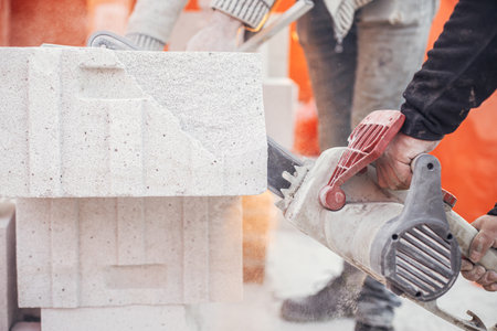 Workers cutting autoclaved aerated concrete block with chainsaw closeup. Builders cutting white blocks for masonry installation. Process of house building at construction site.の写真素材