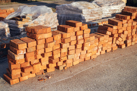 Concrete foundation with bricks for laying. Stack of red bricks on concrete foundation, process of house building. Building materials at construction siteの写真素材