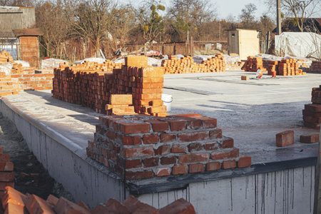 Concrete foundation with bricks for laying. Stack of red bricks on concrete foundation, process of house building. Building materials at construction siteの写真素材