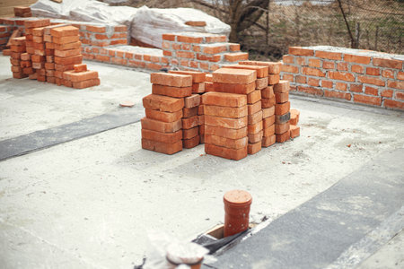 Stack of red bricks on concrete foundation, process of house building. Concrete foundation with bricks for laying. Building materials at construction siteの写真素材