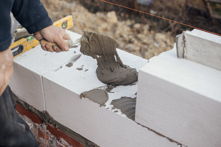 Worker laying autoclaved aerated concrete blocks, working with adhesive and trowel. Builder installing masonry white  blocks close up. Process of house building at construction siteの写真素材