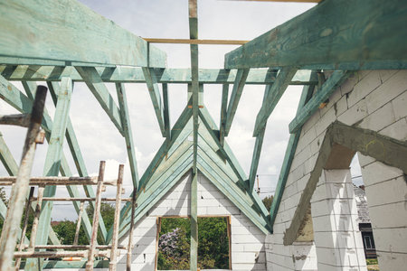 Unfinished roof trusses, view in attic with rafters, beams, windows and chimney. Wooden roof framing. Mansard of modern farmhouse building construction.の写真素材