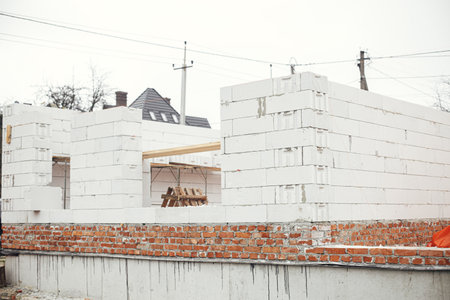 Masonry autoclaved aerated concrete blocks and bricks on concrete foundation. Laying walls with white blocks. Process of house building at construction siteの写真素材