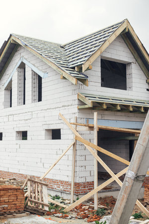 Unfinished house. Wooden roof framing with vapor barrier and dormer on block walls with windows. New modern farmhouse construction. Timber trusses Rafters and beams on aerated concrete blocksの写真素材