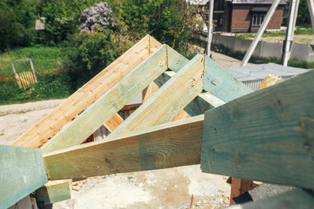 Unfinished roof trusses, view in attic with rafters and beams against sky. Wooden roof framing. Mansard of modern farmhouse building construction.の写真素材