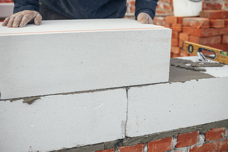 Builder installing masonry white blocks close up. Worker laying autoclaved aerated concrete blocks. Process of house building at construction siteの写真素材