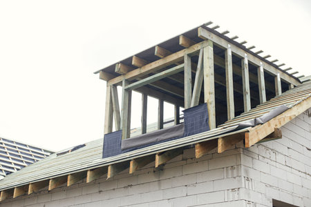 Unfinished house. Wooden roof framing with vapor barrier and dormer on block walls with windows. New modern farmhouse construction. Timber trusses Rafters and beams on aerated concrete blocksの写真素材
