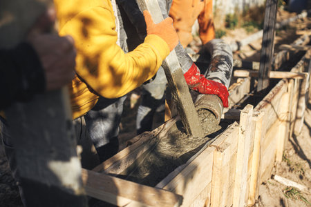 Builders pouring concrete with pump truck in wooden formwork with reinforcement. Workers pouring concrete in formwork for foundation. Construction site, process of house buildingの写真素材