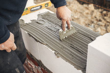 Worker laying autoclaved aerated concrete blocks, working with adhesive and trowel. Builder installing masonry white  blocks close up. Process of house building at construction siteの写真素材